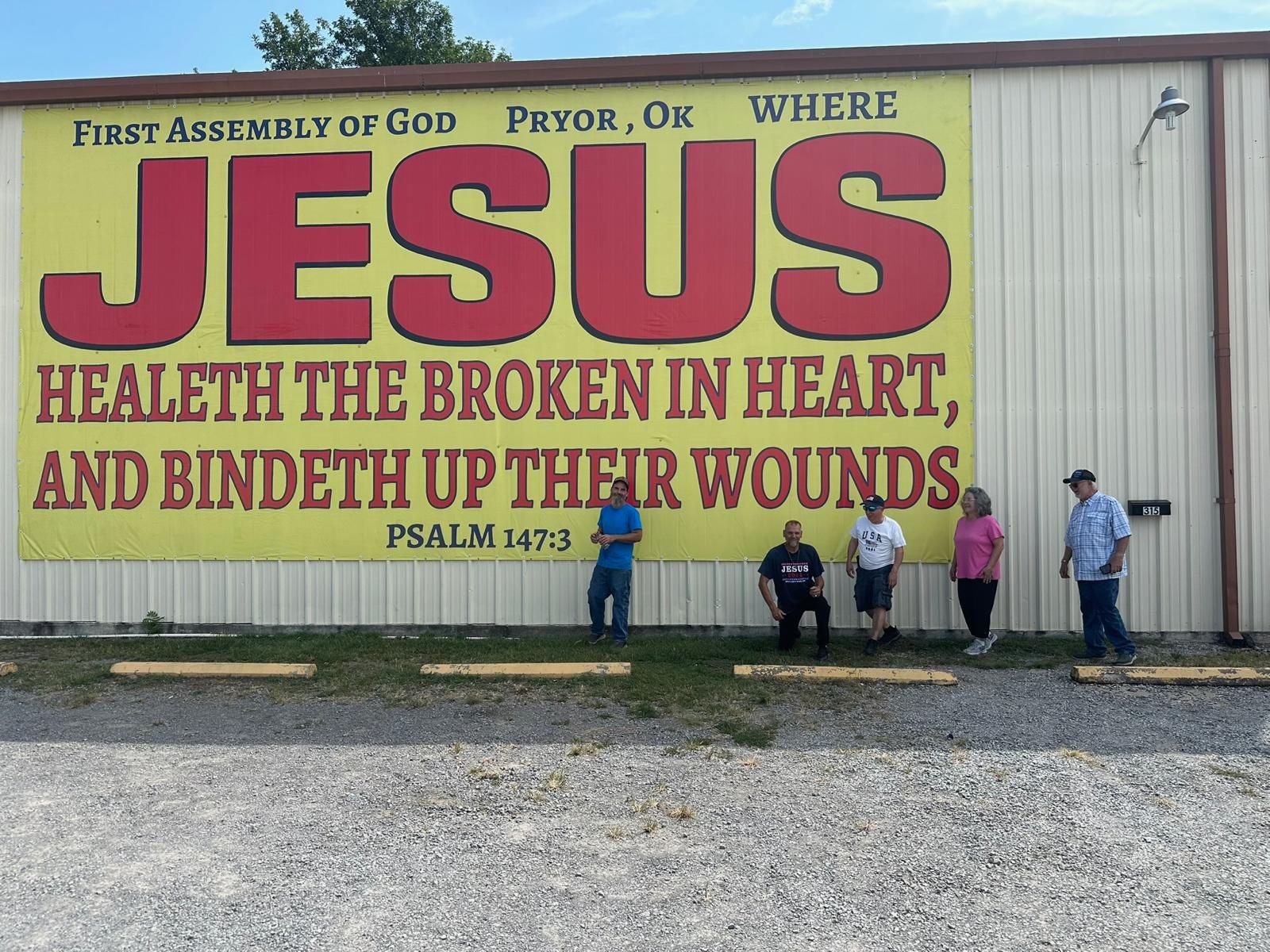 A team standing beside a JESUS banner reading Healeth the broken in heart and bindeth up their wounds, Psalm 147:3, in Pryor, Oklahoma