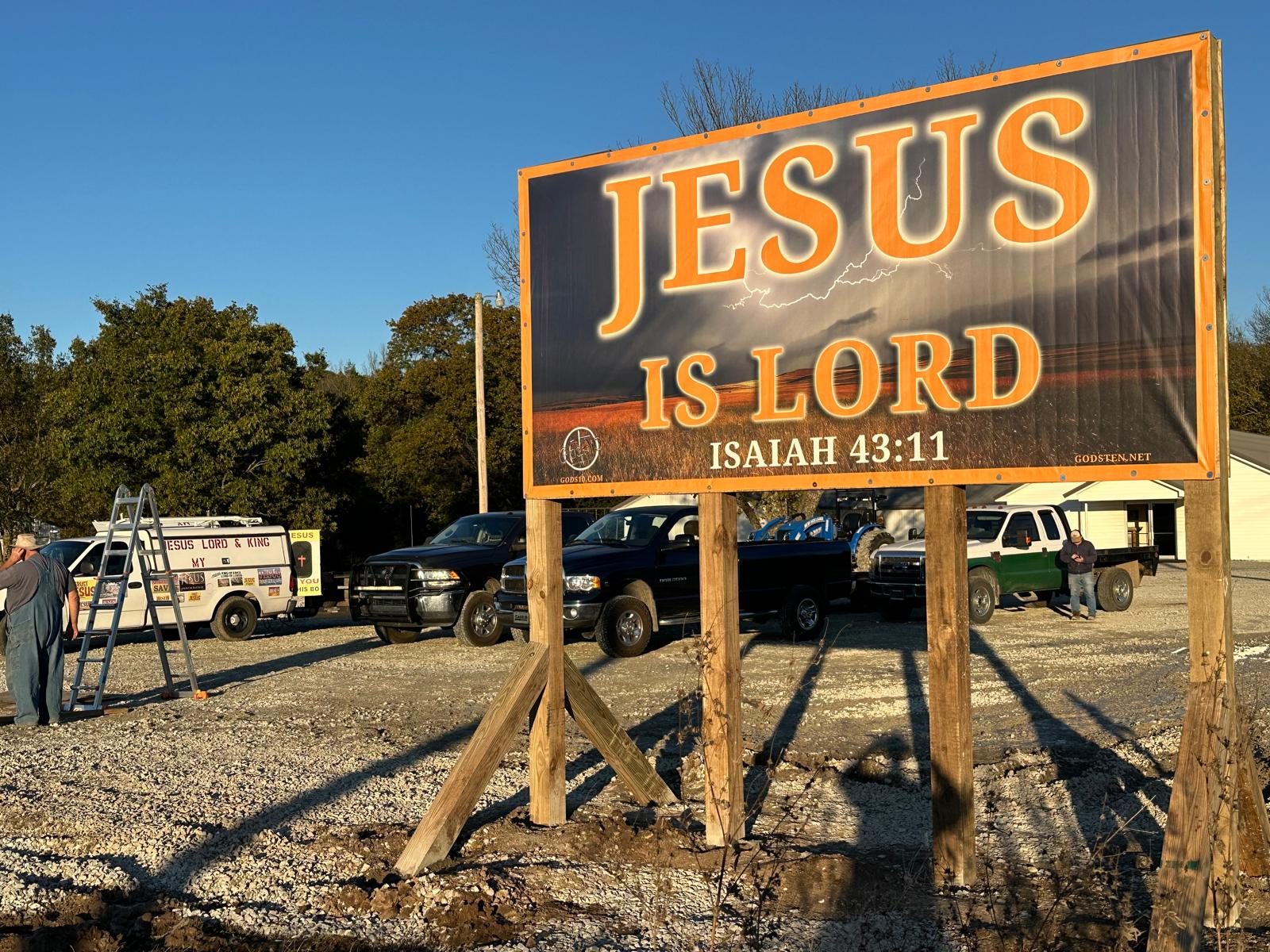 A JESUS IS LORD banner, Isaiah 43:11, raised over a gravel lot